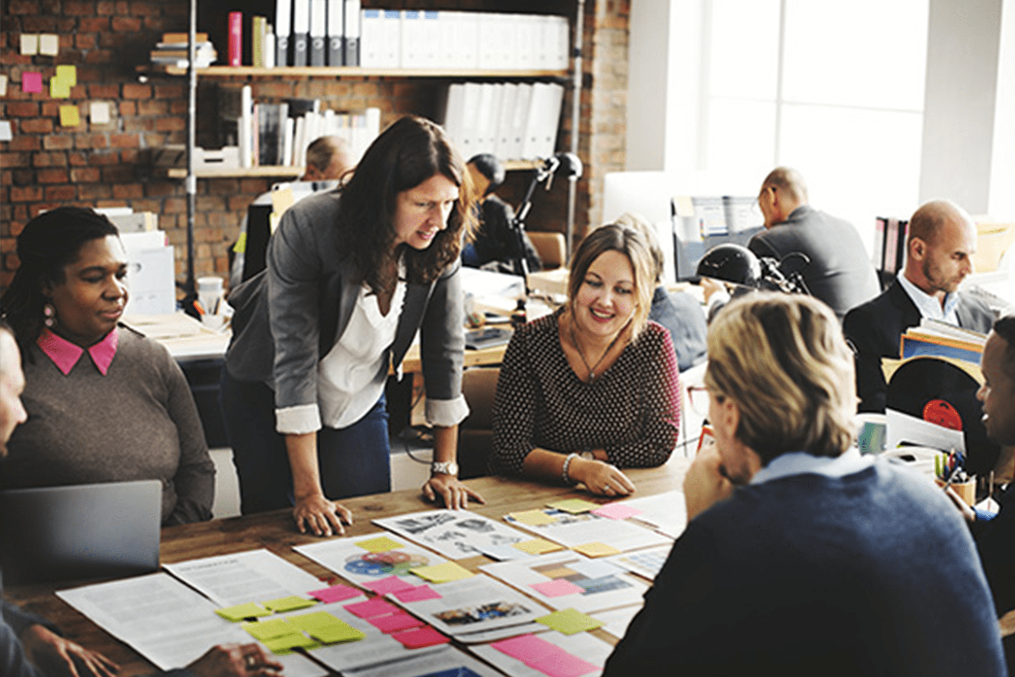 A diverse team discusses ideas at a table covered with documents and colorful sticky notes.