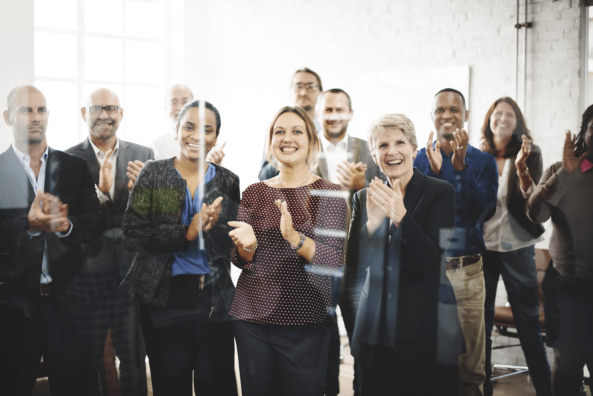 A diverse group of people in business attire stands together, smiling and clapping.